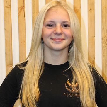 Young woman with long blonde hair smiling in front of wooden panels.