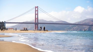 Golden Gate Bridge viewed from a sandy beach with people.