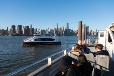 People enjoy a ferry ride with a city skyline in the background.