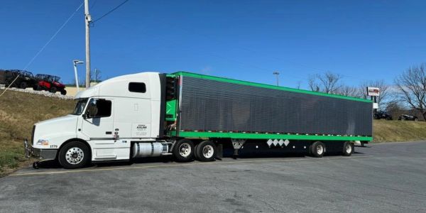 White semi truck with a black and green trailer parked on asphalt.