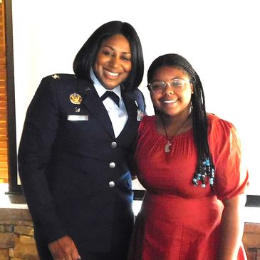 Two smiling women, one in a military uniform and the other in a red dress.