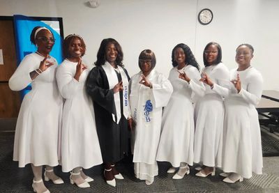 Group of women in white dresses and graduation attire posing indoors.