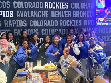 Group of friends posing happily in a sports bar with Colorado team names on the wall.