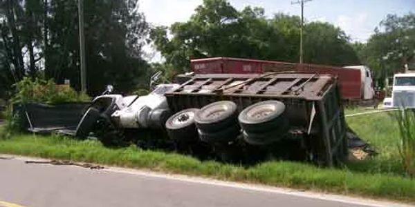 A large truck overturned on the side of a rural road in a grassy ditch.