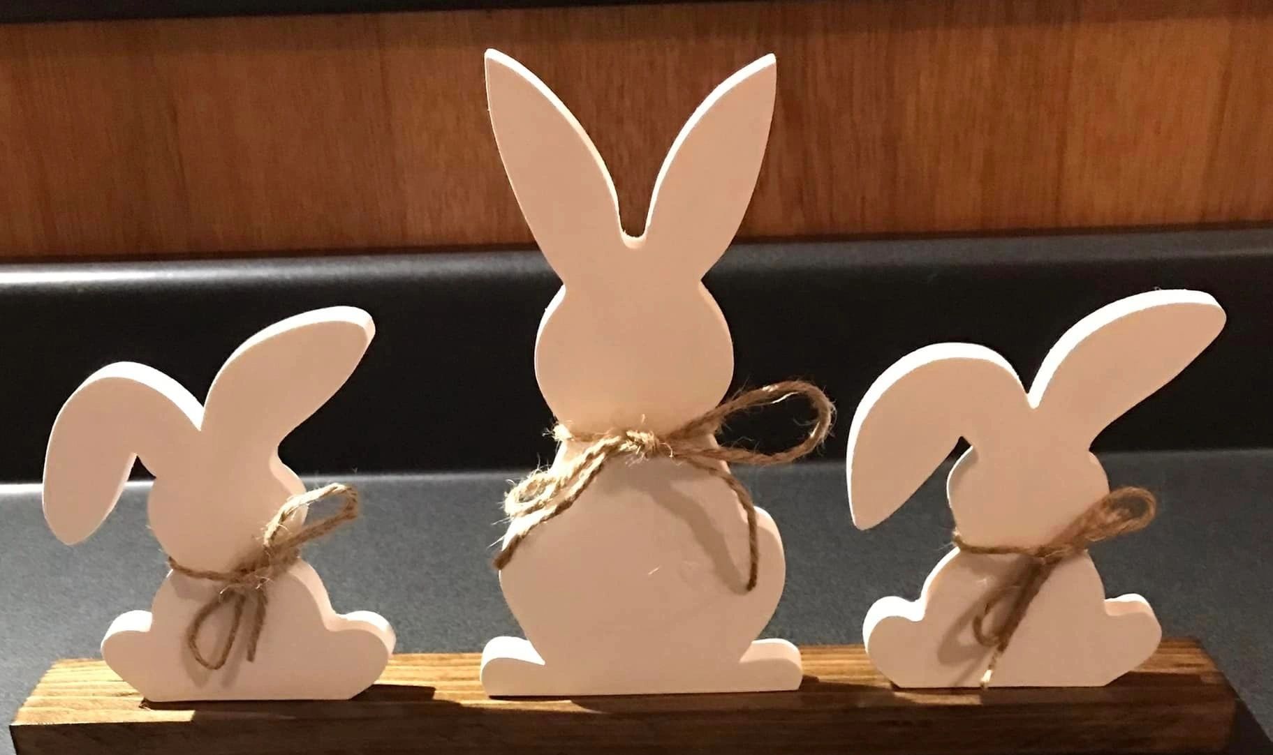 set of 3 white wooden bunnies with string around necks sitting on a piece of wood