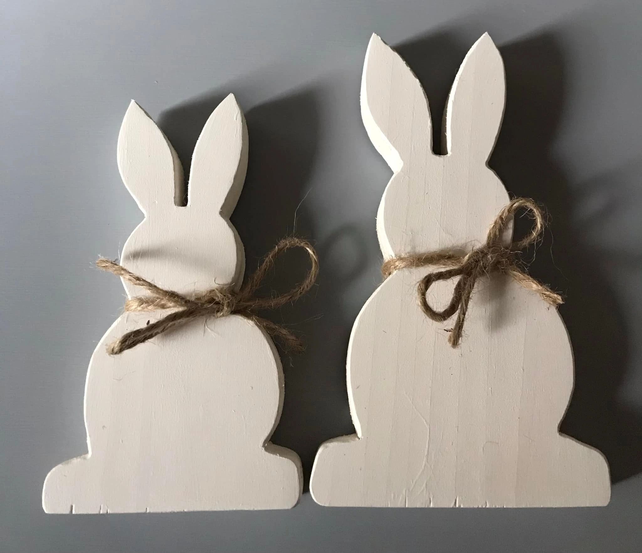 2 white wooden bunnies with brown string tied around necks