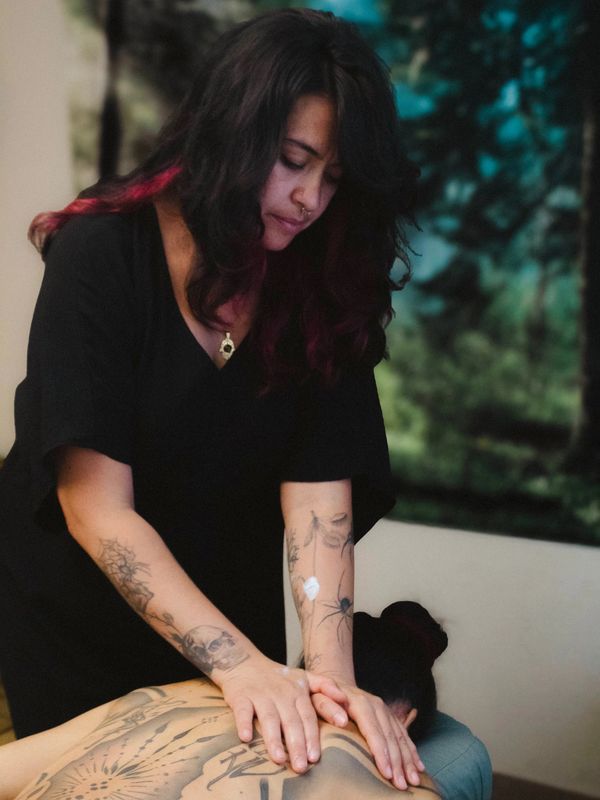 A tattooed woman gives a relaxing back massage indoors.