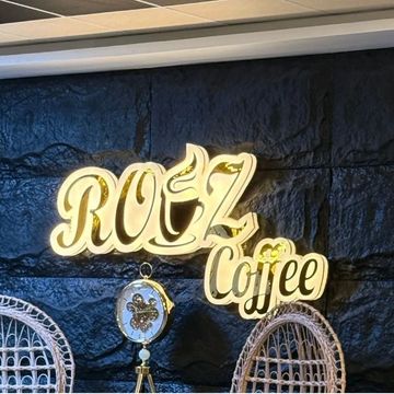 Illuminated ROZ Coffee sign on a textured dark wall above wicker chairs.