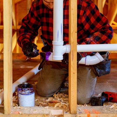 A plumber installs PVC pipes in a wooden frame structure