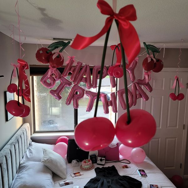 A bedroom decorated with pink cherry-themed birthday decorations and balloons.