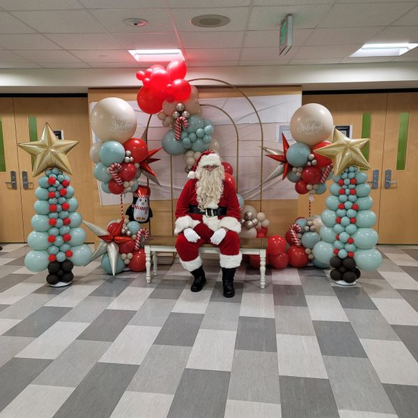 Santa Claus sitting on a bench surrounded by festive balloon decorations.