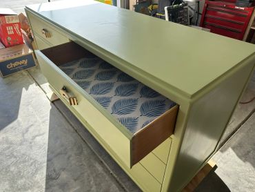 Green dresser with open drawers lined with leaf-patterned paper.