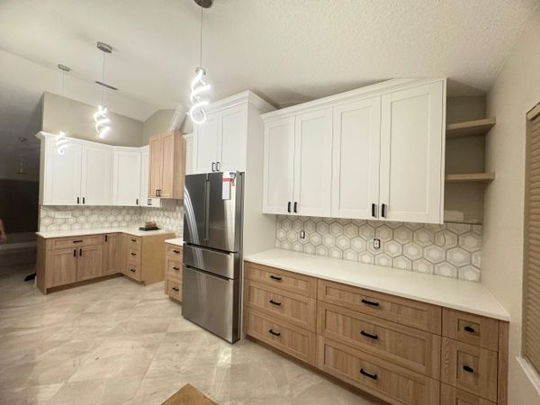 Modern kitchen with white upper cabinets, wood lower cabinets, and hexagonal tile backsplash.