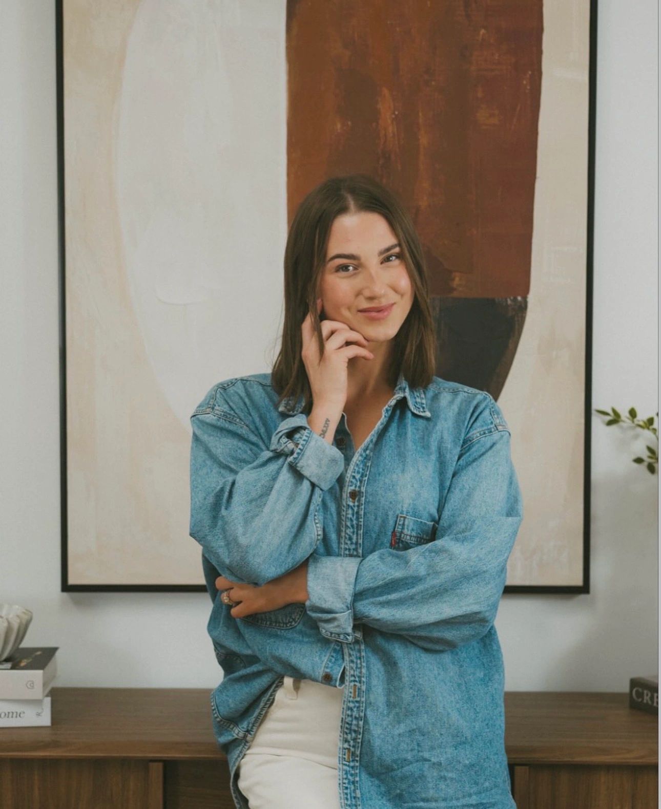 Smiling woman in denim shirt poses confidently indoors.