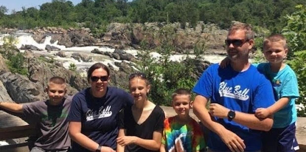 Family posing happily by a scenic waterfall and rocky landscape.