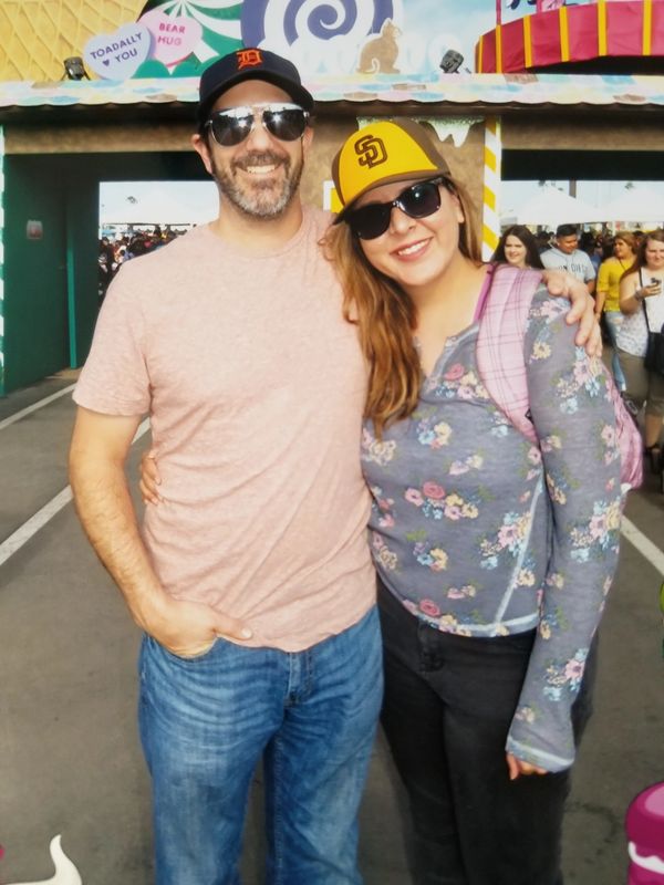 Darren and Adriana smiling arm-in-arm at a fair, wearing Detroit Tigers and San Diego Padres caps - 