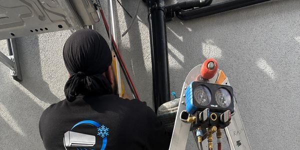 Technician working on HVAC equipment with gauges on a ladder.