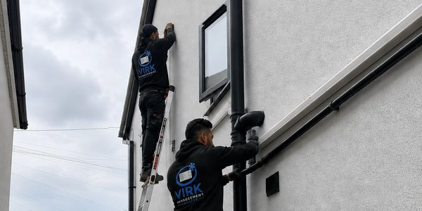 Two technicians in black jackets working on a building exterior.