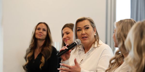A woman speaking into a microphone during a panel discussion with other women.
