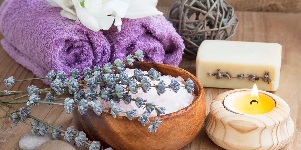 Spa setting with lavender, towels, candle, and bath salt for relaxation.