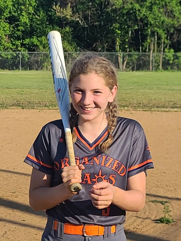 Young girl smiling with a baseball bat on a field.