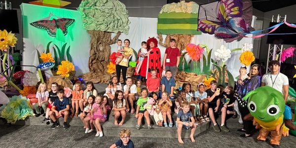 Group of children and adults in colorful bug-themed costumes and decorations.