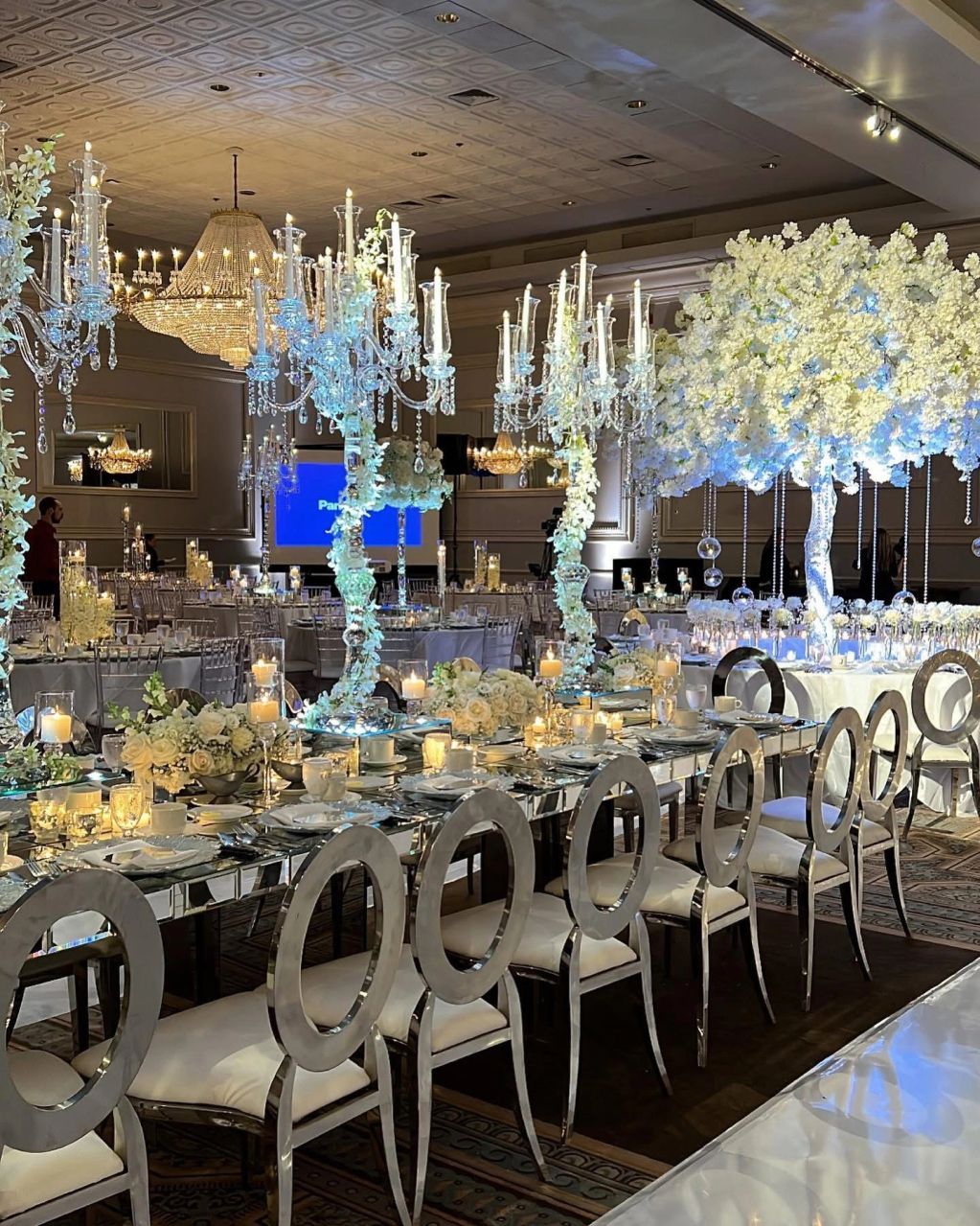 Elegant wedding reception with mirrored tables, white floral arrangements, and crystal chandeliers.