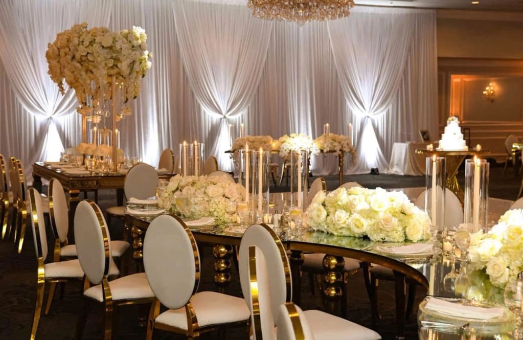 Elegant wedding reception setup with white floral arrangements and gold-accented chairs.