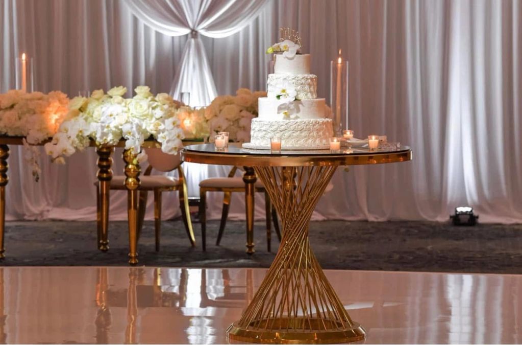 Elegant white wedding cake on a gold table with floral decorations and candles.