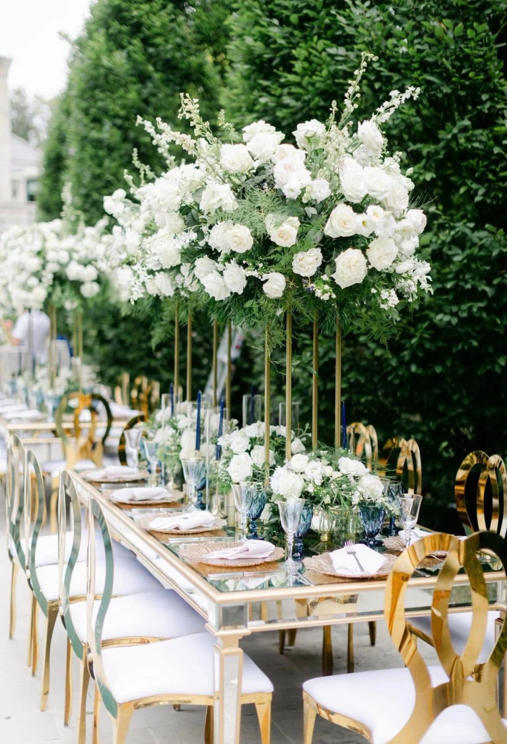 Elegant outdoor dining setup with white floral centerpieces and gold chairs.