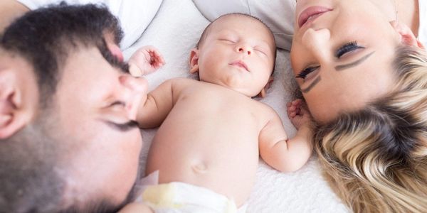 Mother and father in bed with infant, eyes are closed, enjoying the moment.