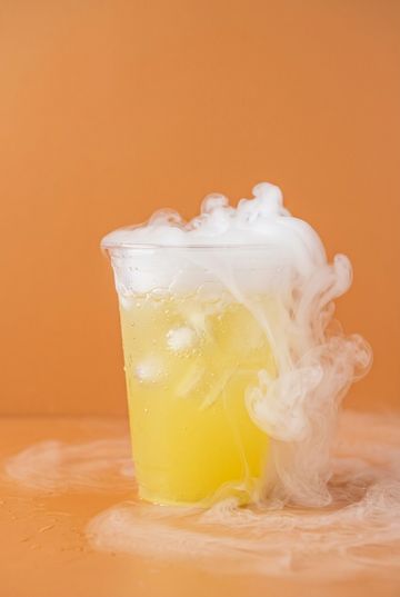 Yellow drink with ice and smoky fog effect in a clear cup.