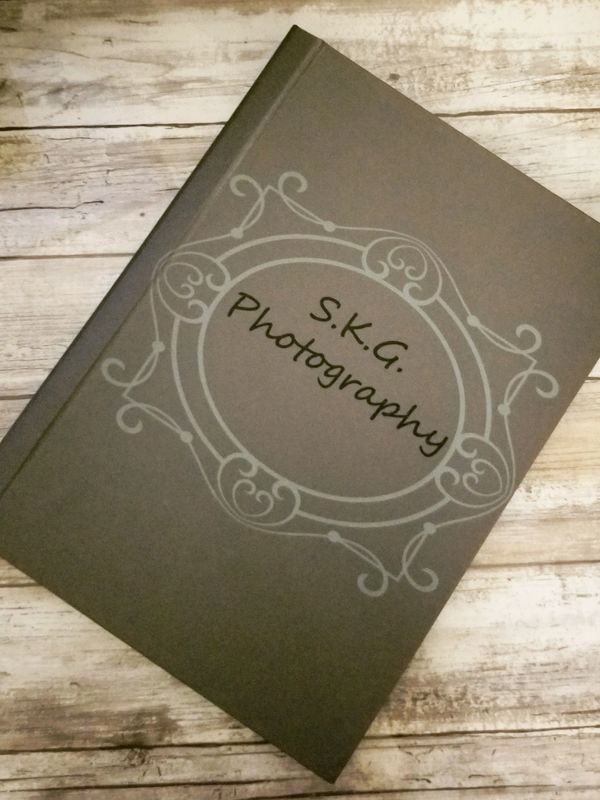 A gray photo album titled 'S.K.G. Photography' on a wooden surface.