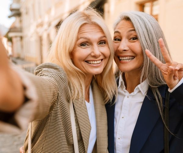 Two happy women taking a selfie outdoors, one showing a peace sign.