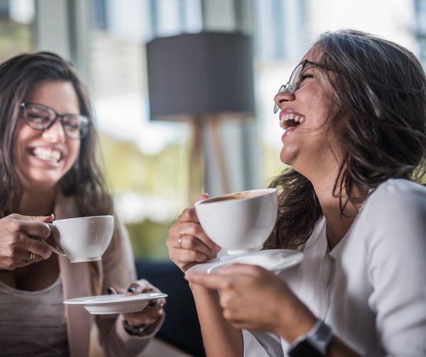 Two women enjoying coffee and laughing together indoors.