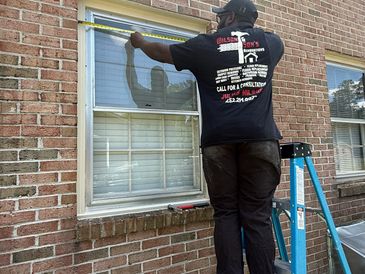 Worker measuring a window frame on a brick house for installation.