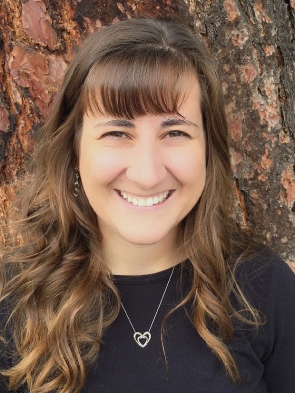Smiling woman with wavy hair in front of a tree bark background.