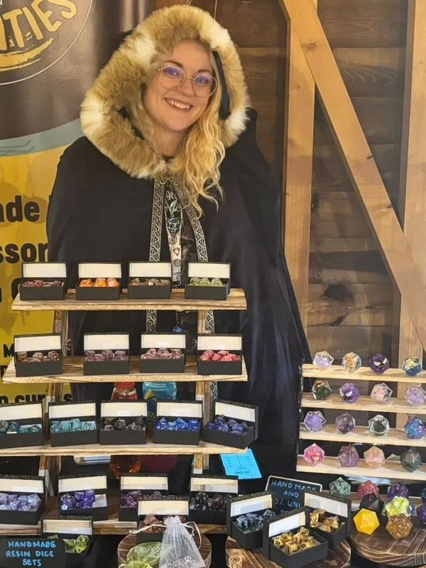 Vendor smiling behind a table of handmade tabletop gaming accessories and dice sets.