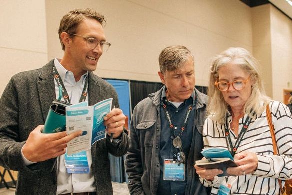 Drew Gottenburg standing with a man and woman reviewing a pamphlet together.