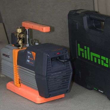 Compact Hilmor vacuum pump with carrying case on a table.