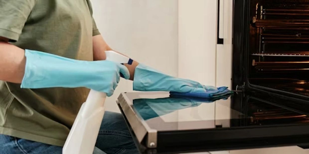 lady in blue gloves holding spray bottle and wiping open oven door 