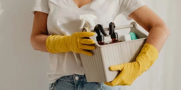 girl in yellow gloves holding caddy with cleaning products and spray bottles