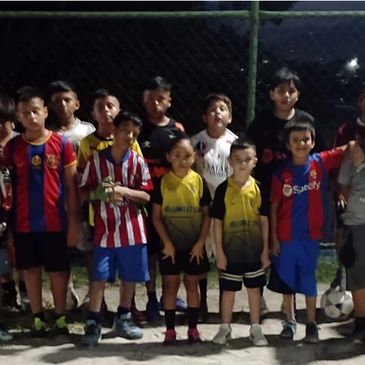 A group of young boys posing in soccer jerseys at night on a field.