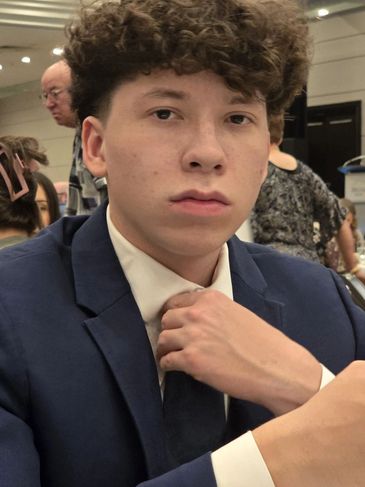 Young man in a blue suit adjusting his tie at an event.