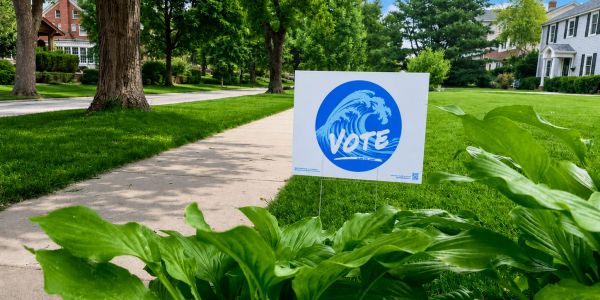 Yard sign with a vote message near a sidewalk.