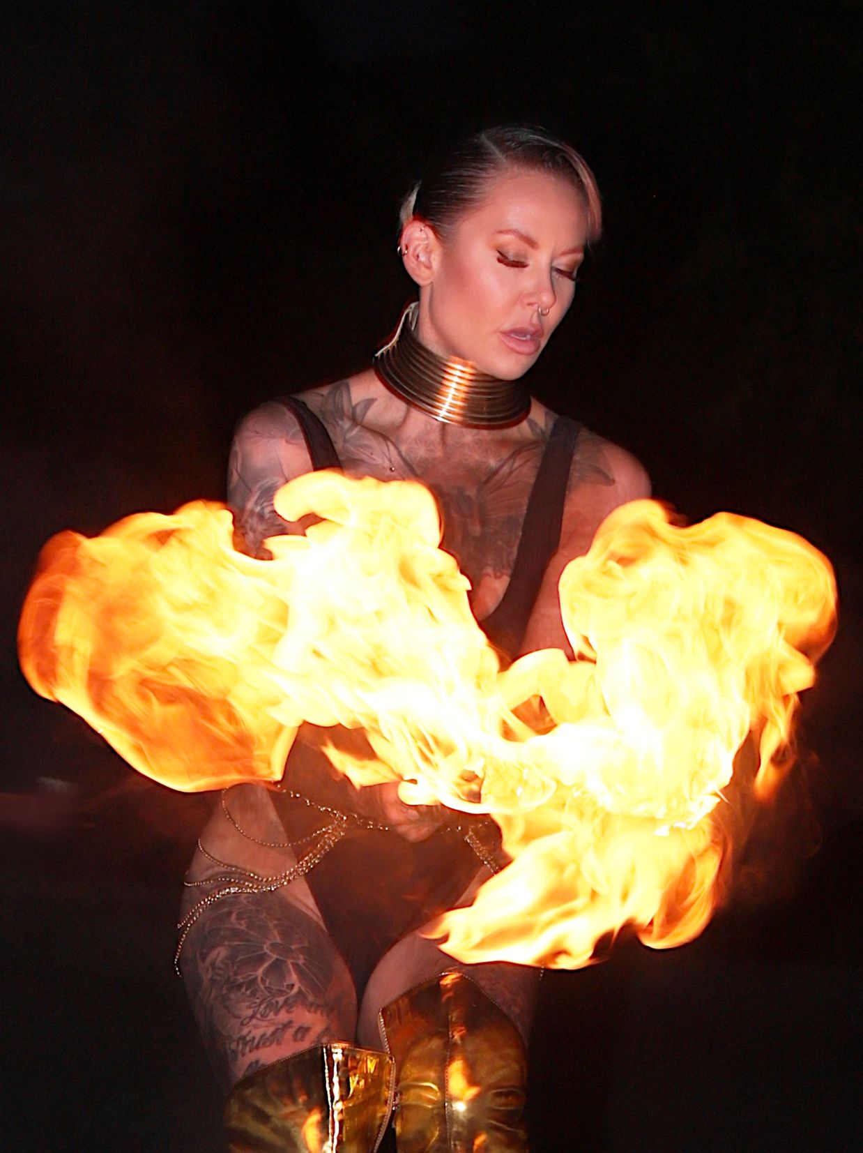 A woman performs fire dancing, creating large flames at night.