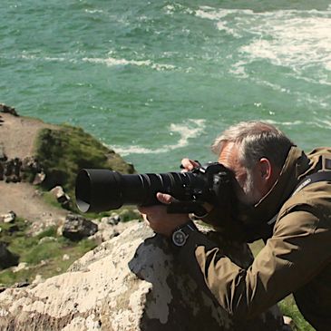 Photographer with a large lens capturing nature by the ocean cliffs.