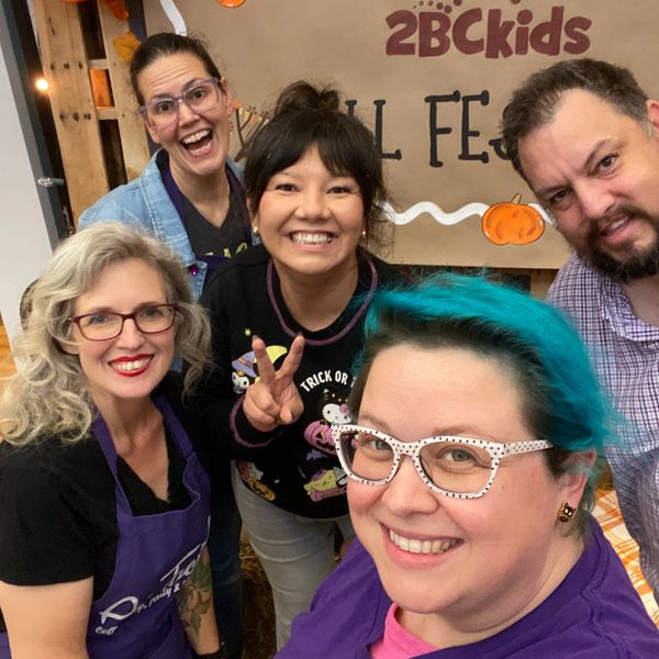 Five smiling friends pose together at a festive event with Halloween decorations.