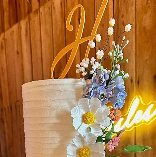 White cake with floral decoration and golden topper.