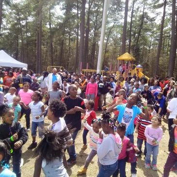 Children and adults gathered at an outdoor event with a playground in the background.